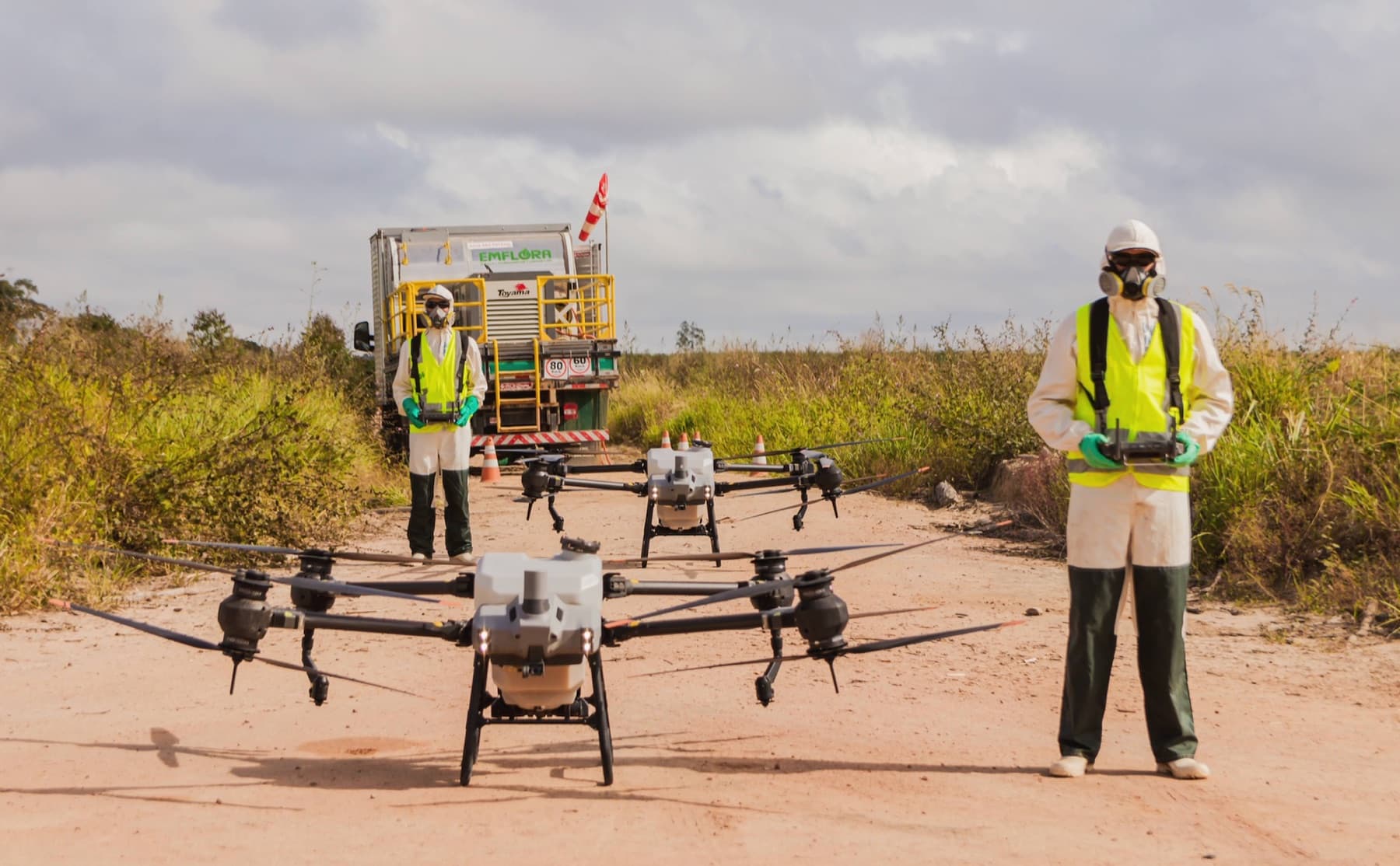 Drone de pulverização da Emflora em voo, com operador de EPI e caminhão de apoio